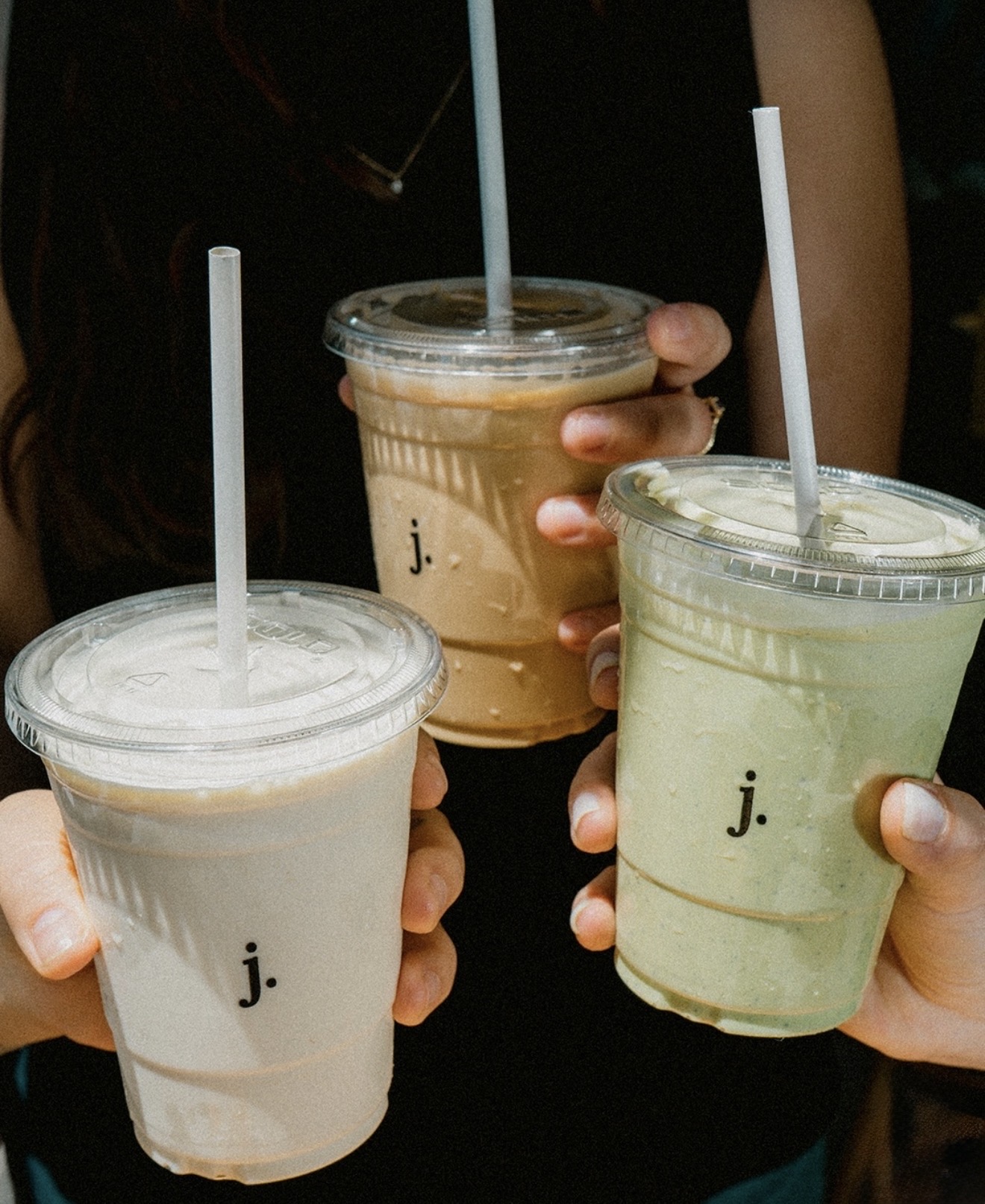 Tres malteadas en vasos con la letra j., sostenidas por dos personas